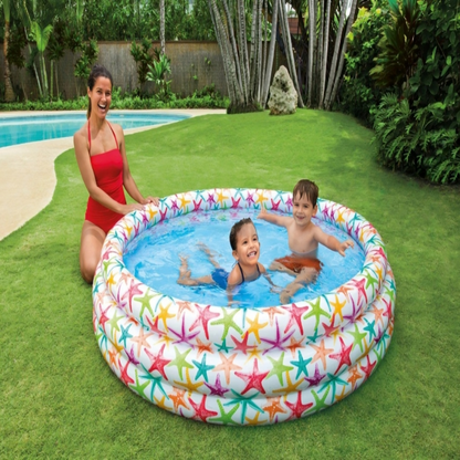 Woman and two children playing in a colorful inflatable pool on grass